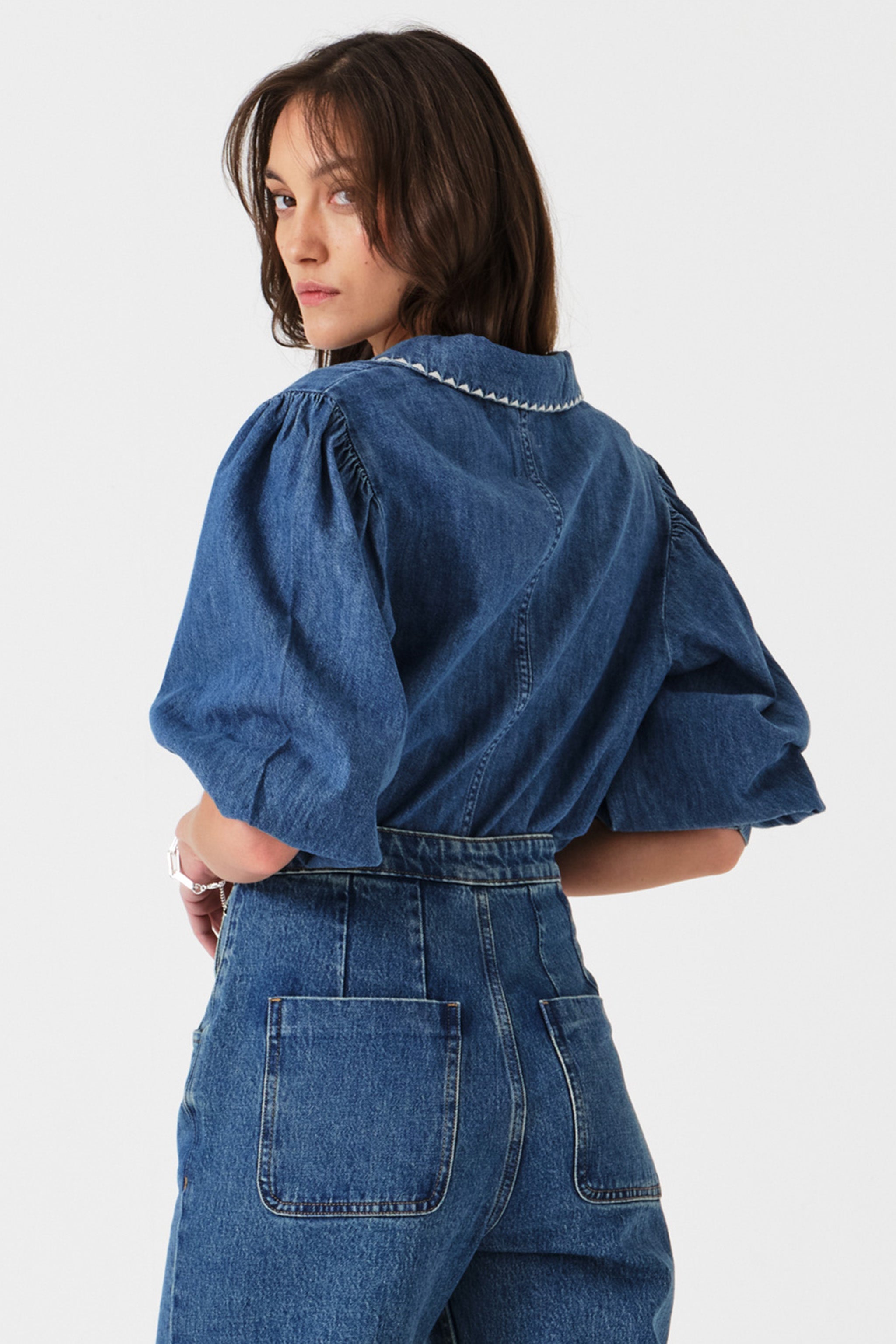 Woman showing the back of a blue denim button up top with oversized collar