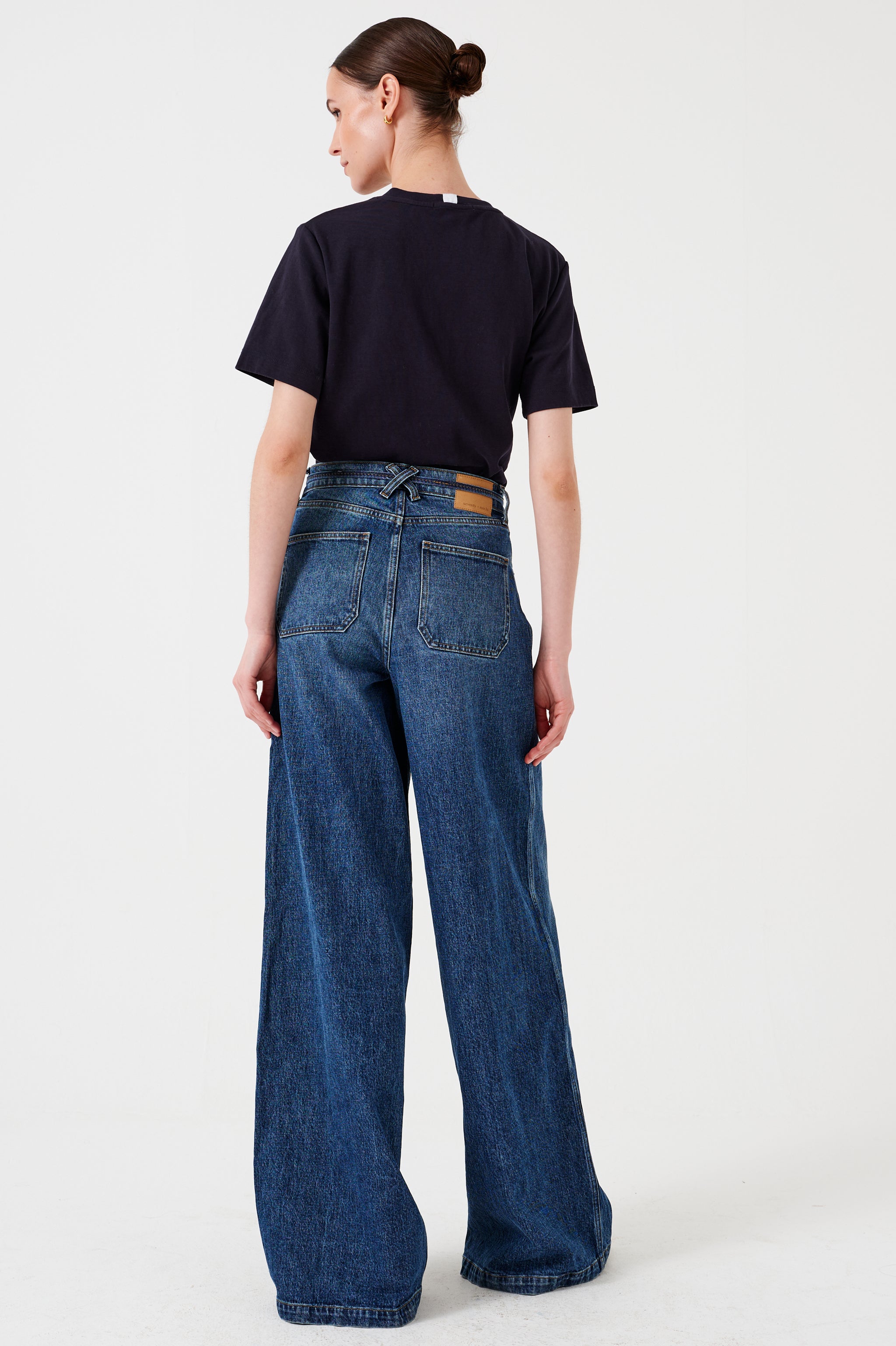 Woman wearing a black t-shirt and blue wide-leg jeans with a tie waist string detail on a white background