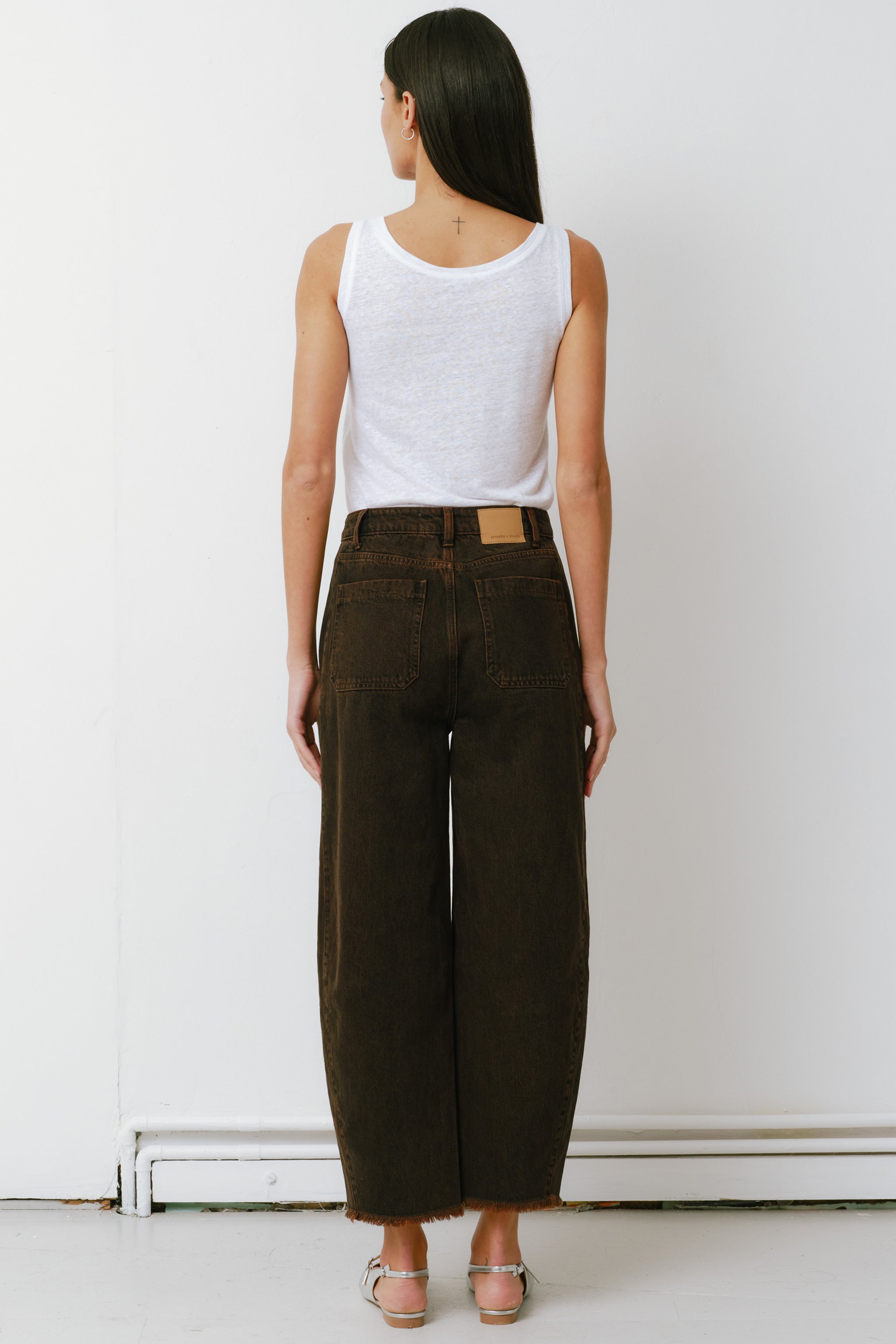 woman standing against a white background wearing high-rise dark brown cacao-colored carpenter barrel leg jeans with a frayed hem and a white top.