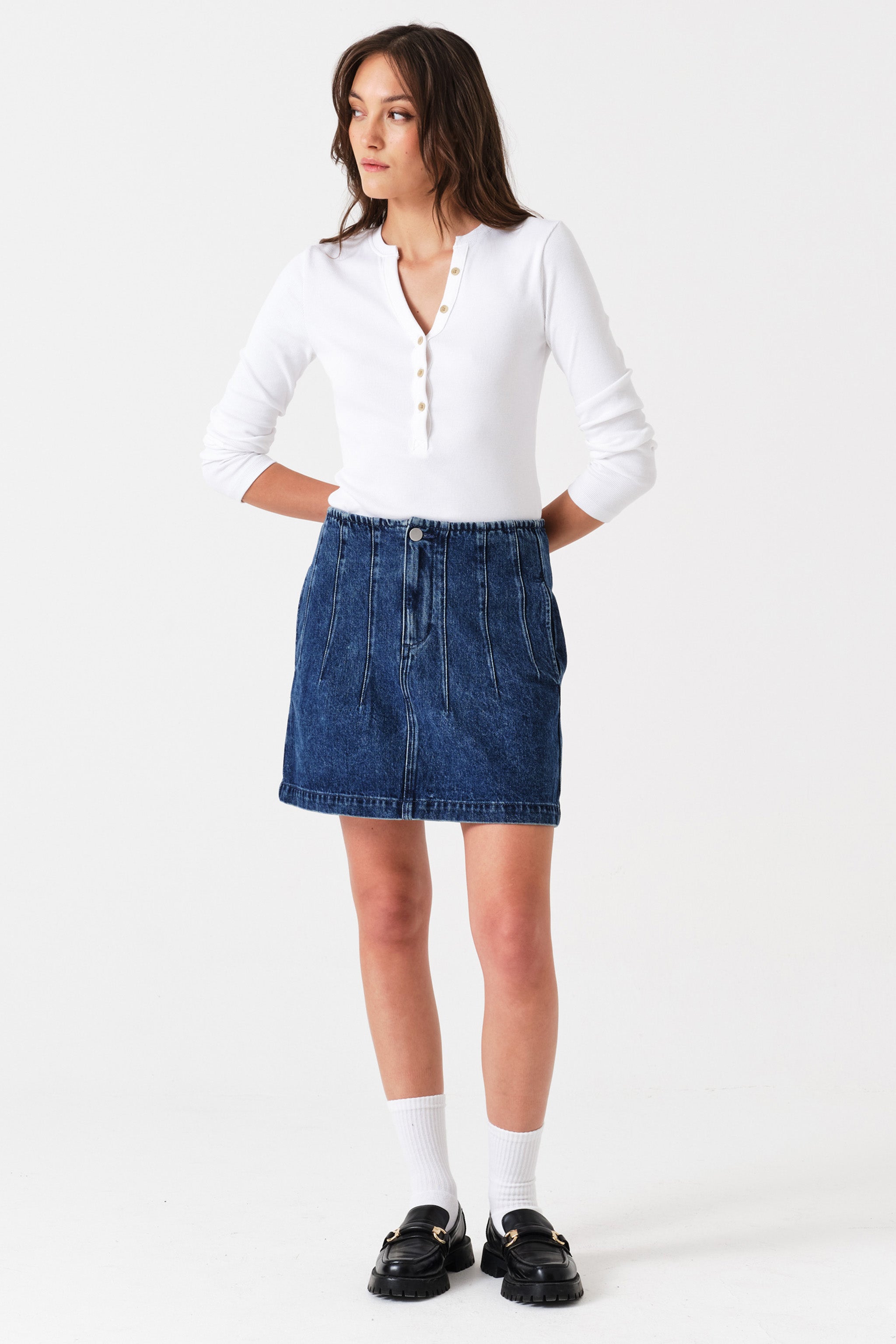 Woman wearing a dark blue denim mini skirt with seam details and a white shirt on a white background