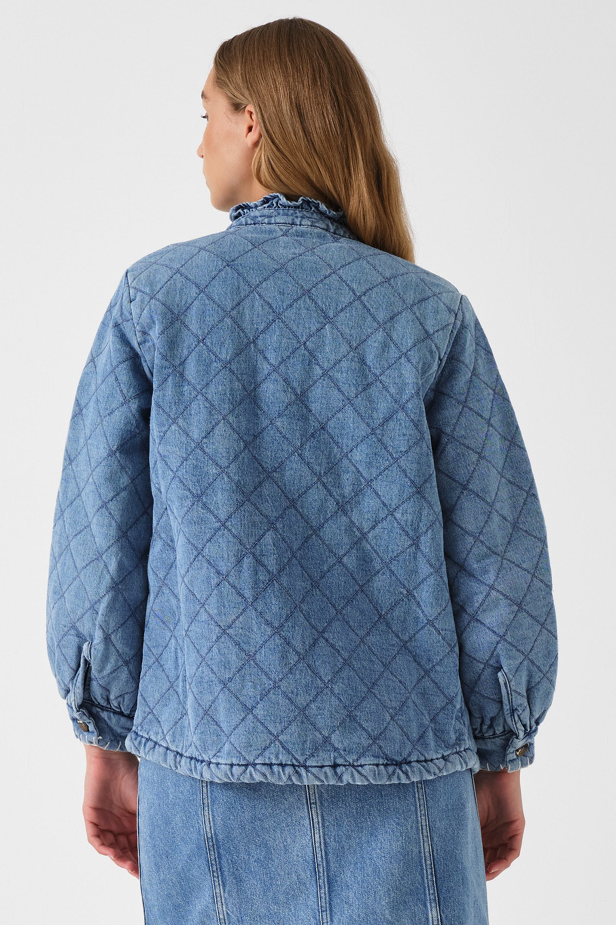 Woman showing the back of a light blue quilted denim jacket on a white background