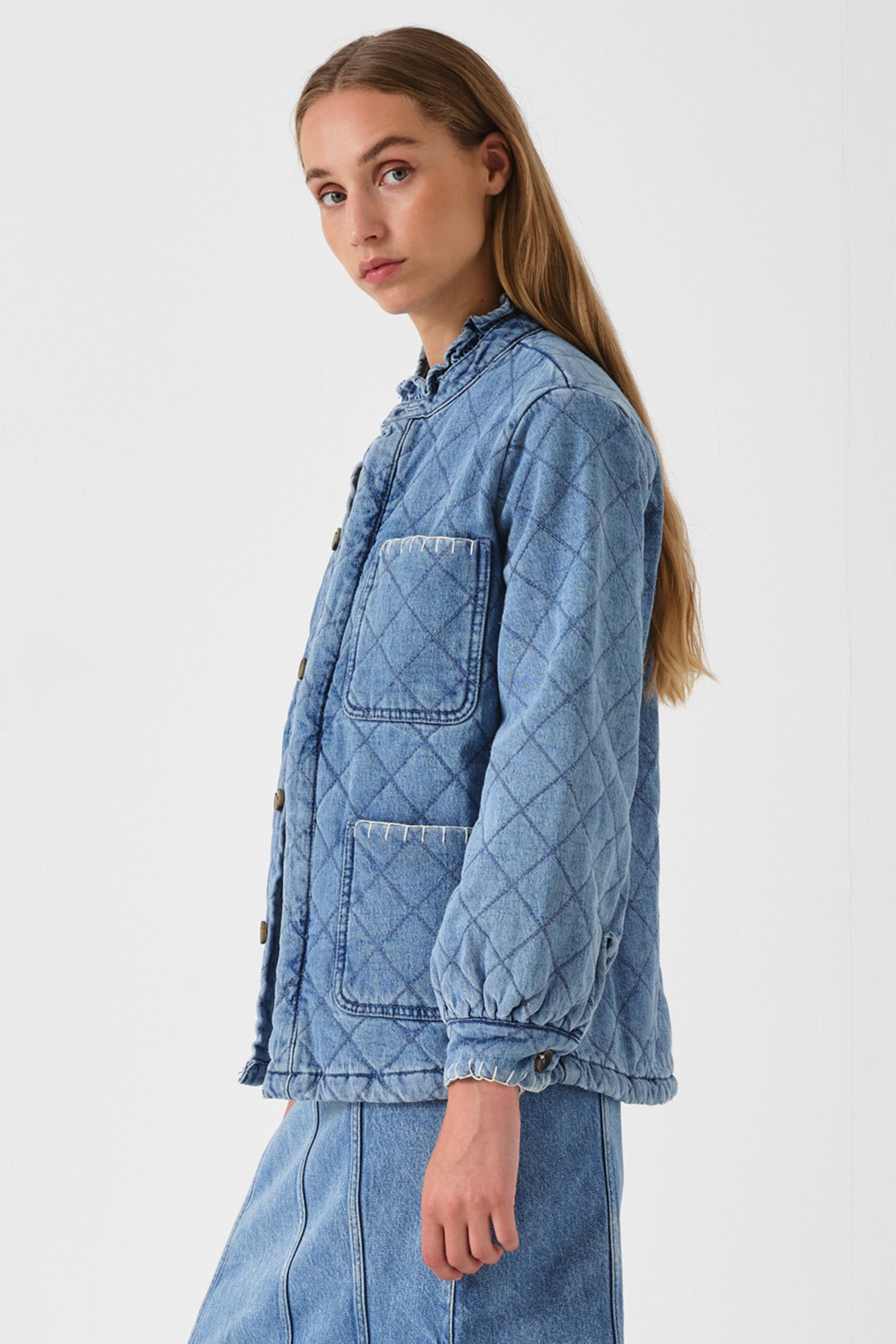 Woman showing the side of a blue quilted denim jacket on a white background