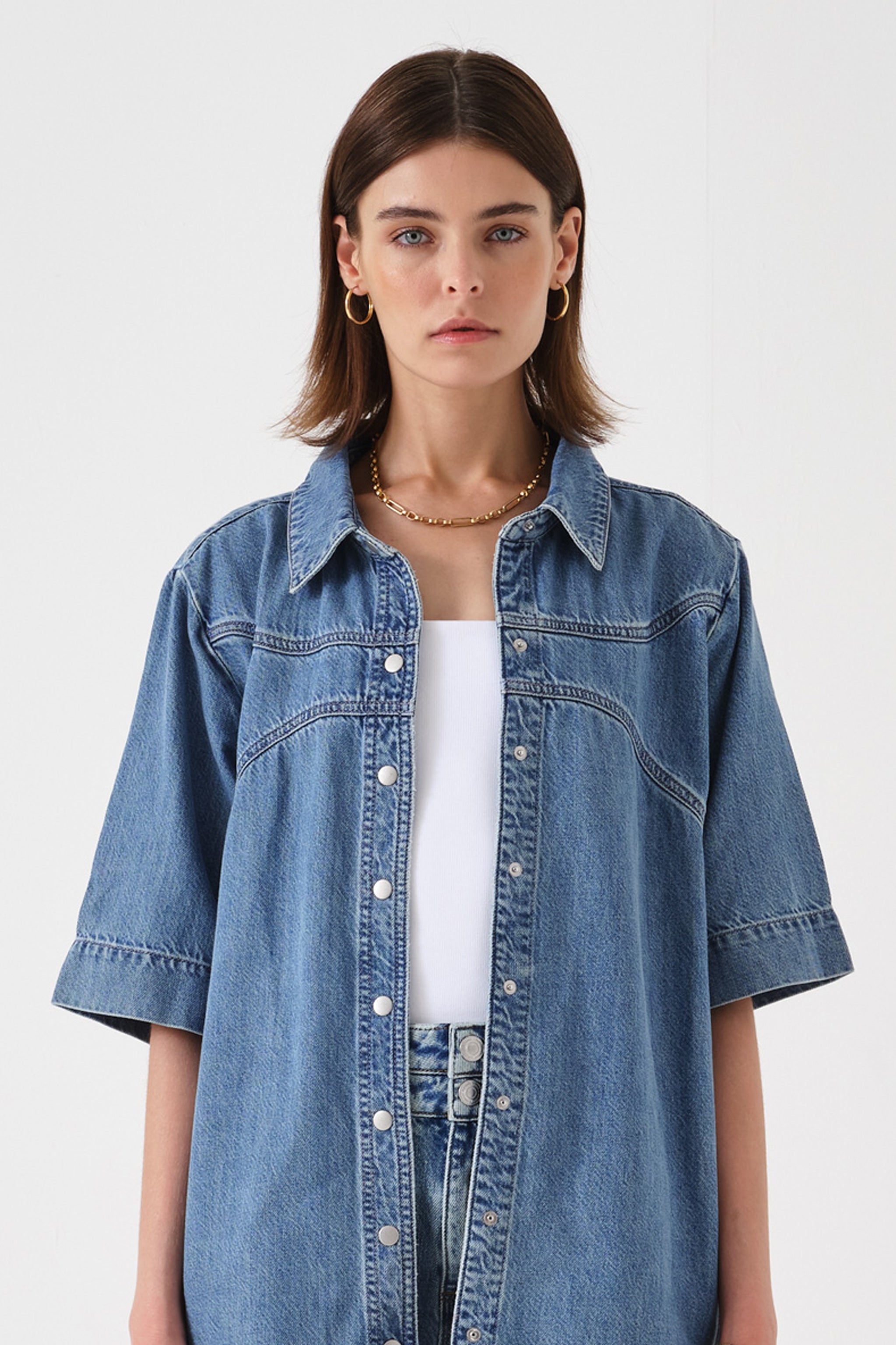 Woman wearing a blue denim shirt over a white top on a white background