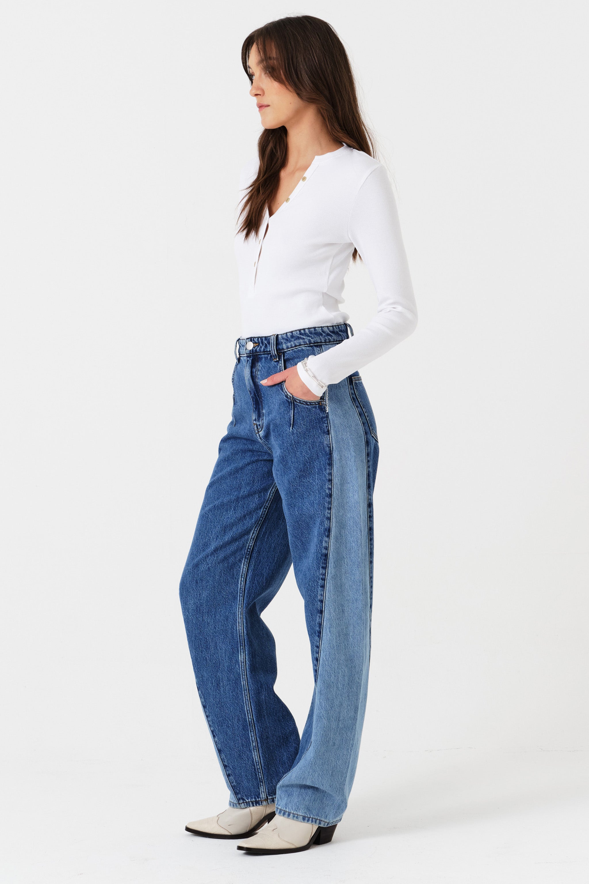 Woman wearing two toned blue barrel leg jeans and a white shirt on a white background photographed from the side