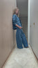 woman wearing a blue denim jacket with a frill collar, white stitch detailing, button-up front, and four large pockets with blue jeans